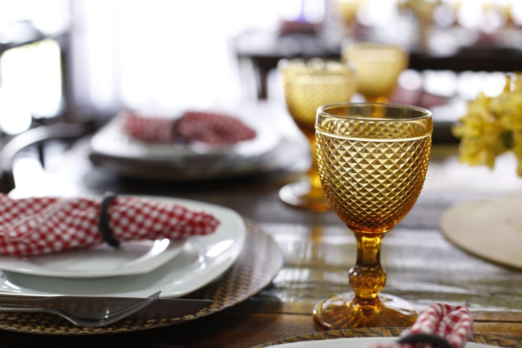 Sophisticated table setting with amber goblets and red checkered napkins on a wooden table.