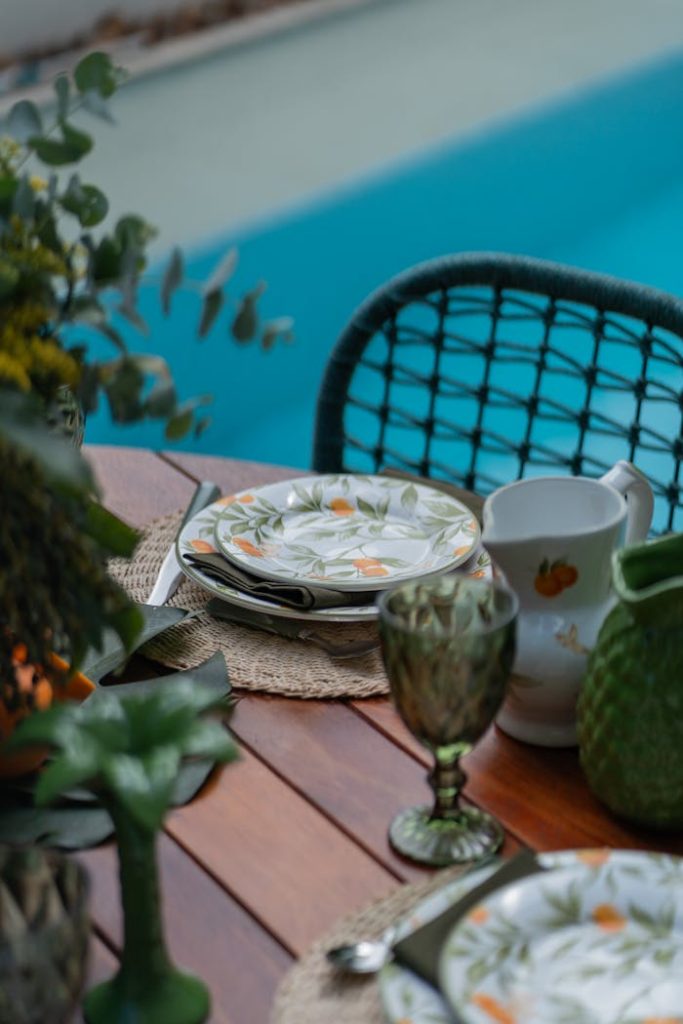 Elegant tableware arrangement by the poolside, featuring floral patterns and lush greenery.